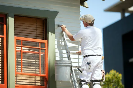 Painter brushing wood siding on a beach cottage with colorful trim